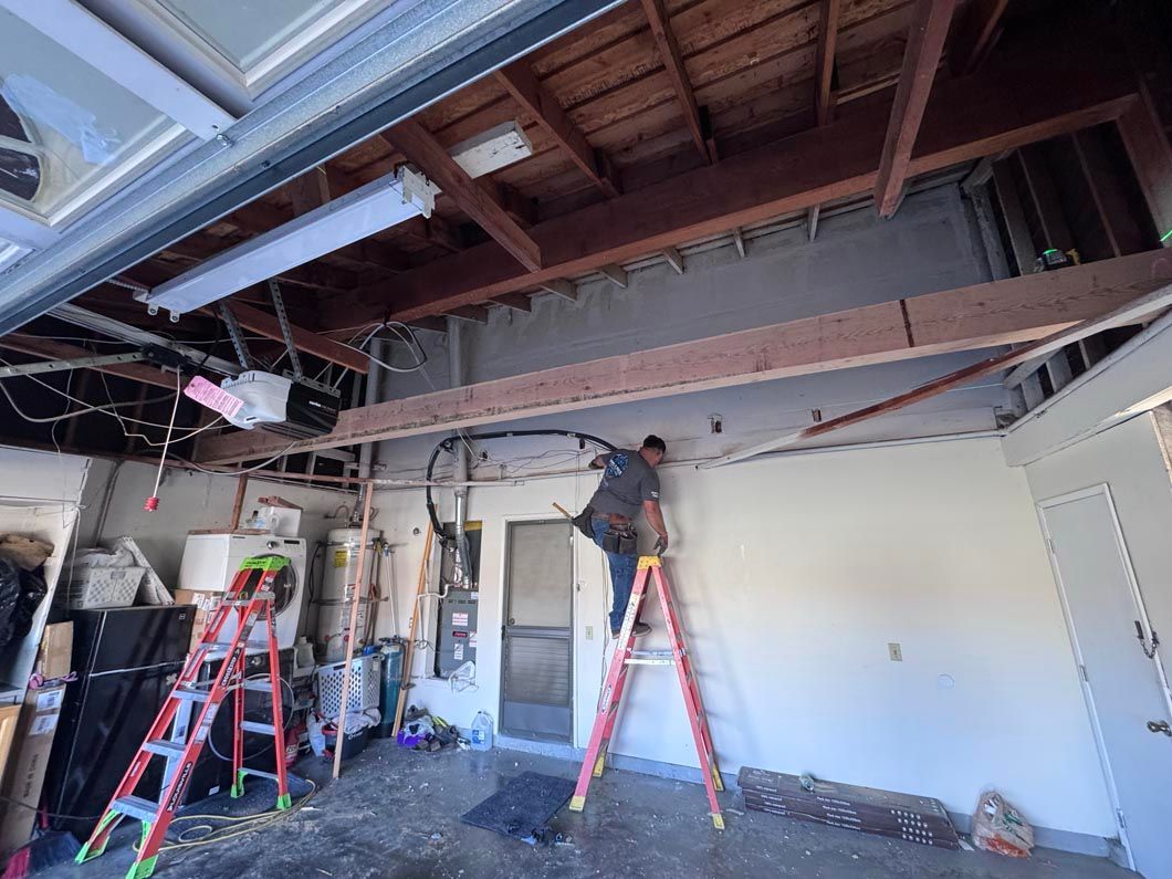 Two workers on ladders repairing a ceiling in a warehouse-like interior with exposed beams and tools.