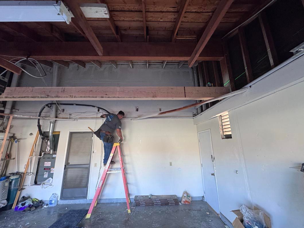 Worker on red ladder repairing exposed ceiling in unfinished room with white walls and open rafters