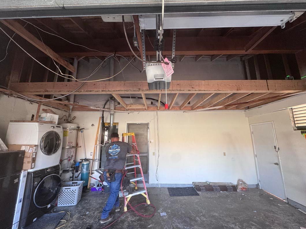 Cluttered garage interior with exposed ceiling beams, ladders, tools, and a bicycle along the wall