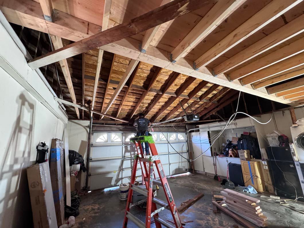 Worker on a red ladder in a room with exposed ceiling beams and scattered construction materials.