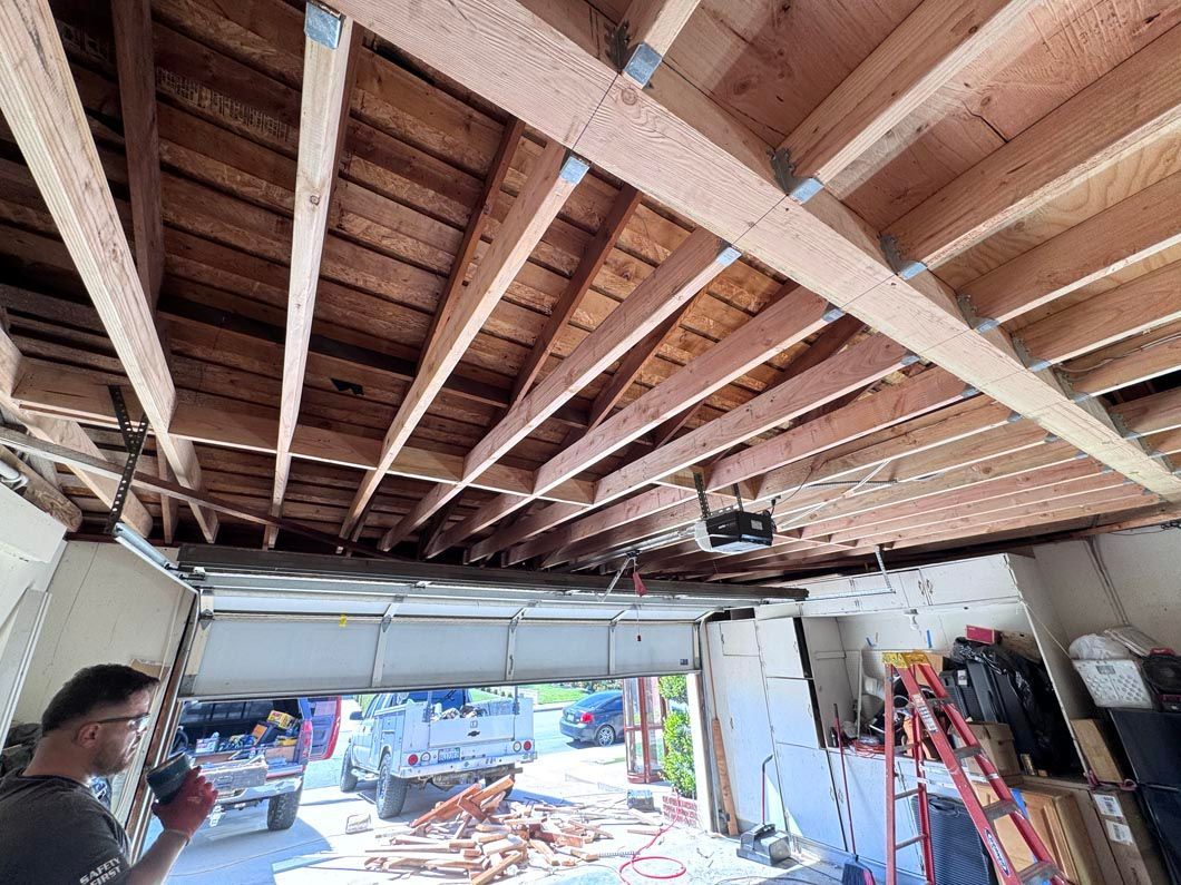 Exposed wood ceiling in a garage under renovation, with tools, ladders, and daylight at the open entrance.