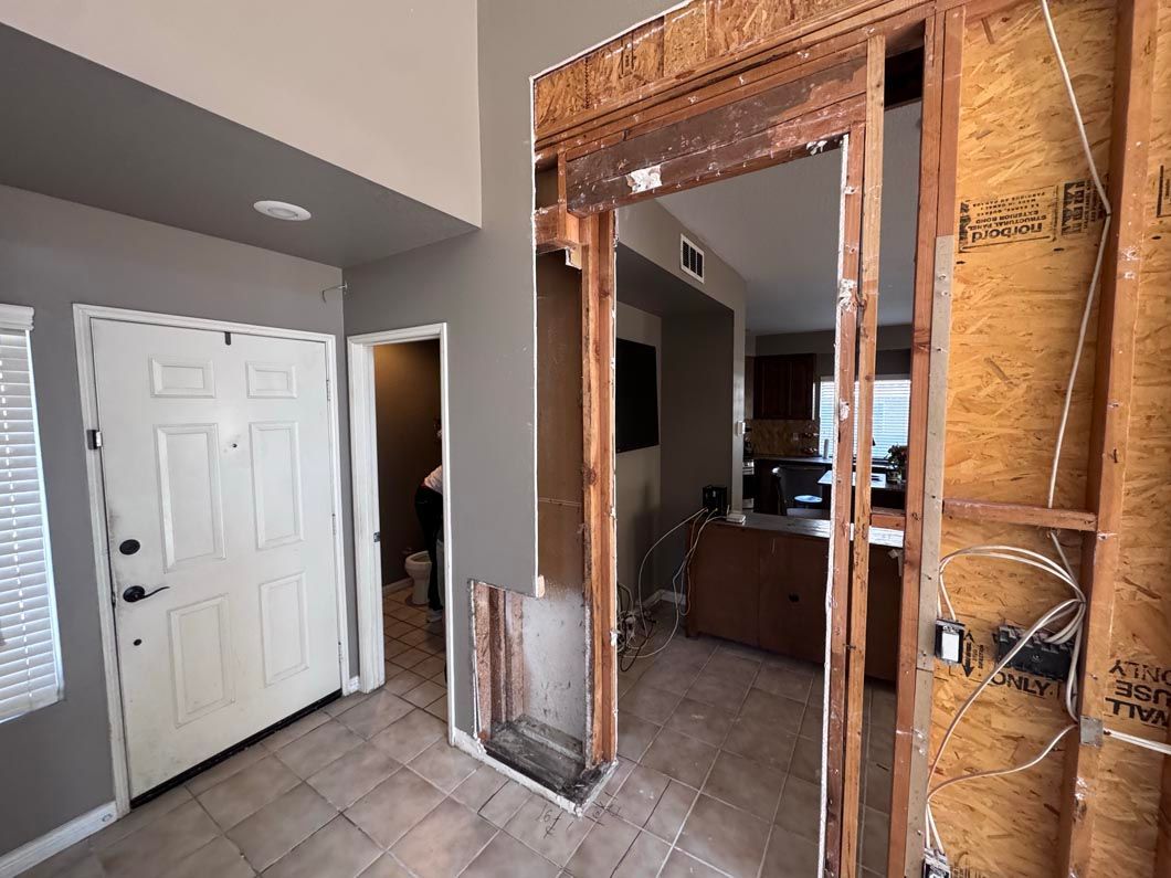 Interior hallway under renovation with exposed studs, a doorway, and white closet doors on tiled floor.