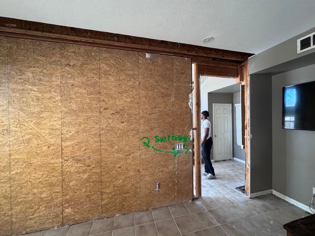 Empty room with plywood-covered wall and a person standing in a doorway near a TV