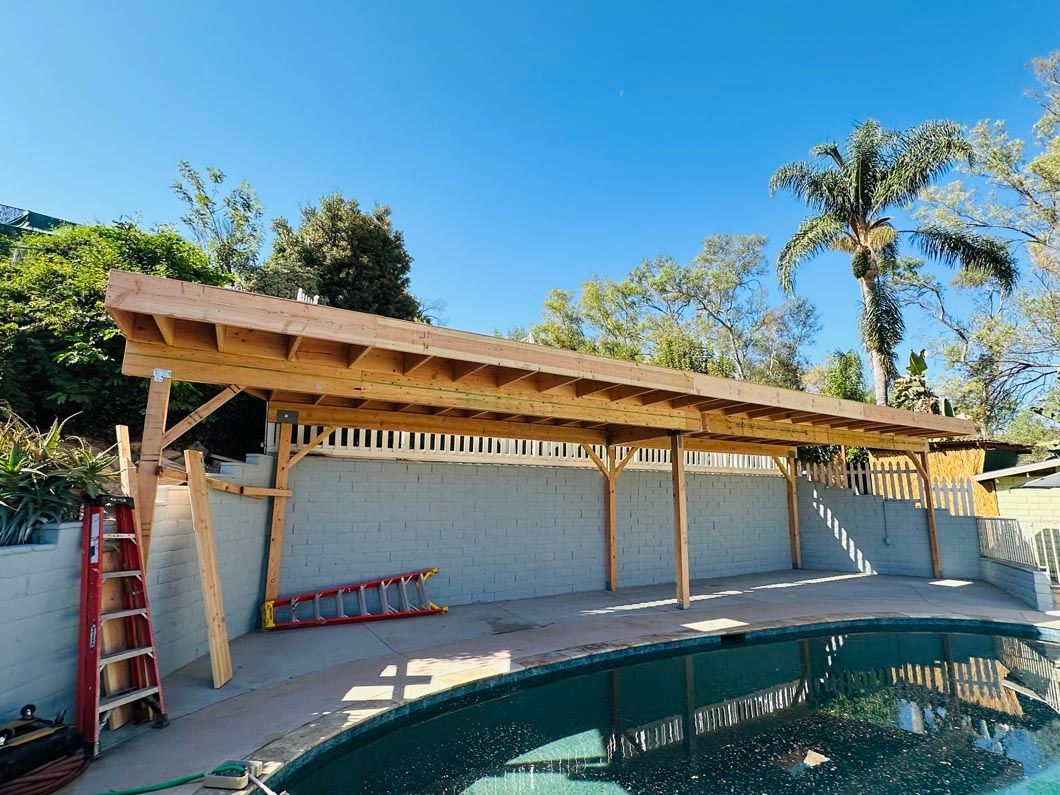 Backyard pool beside a long wooden pergola and white wall under a clear blue sky