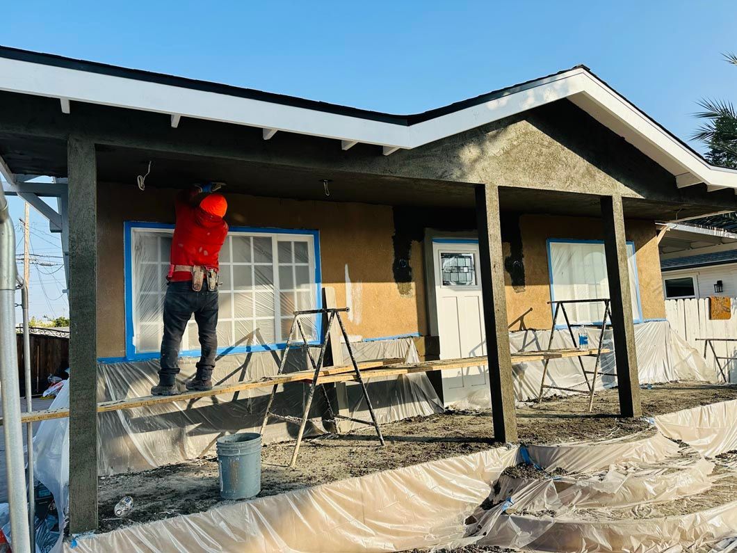 Worker painting a house exterior on a construction site with scaffolding and tarp-covered ground
