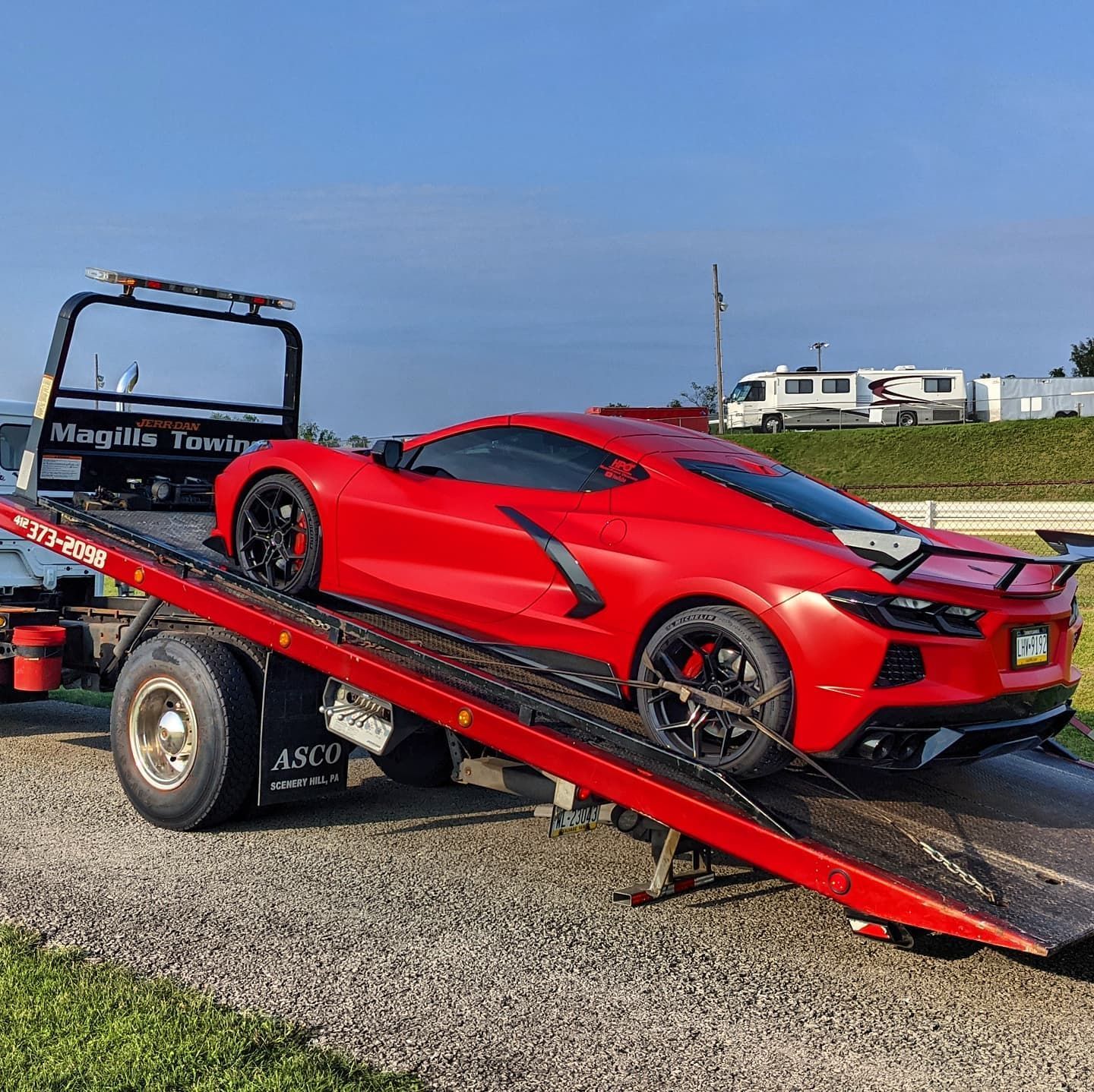 Red sports car on a tow truck ramp in a gravel lot under a blue sky