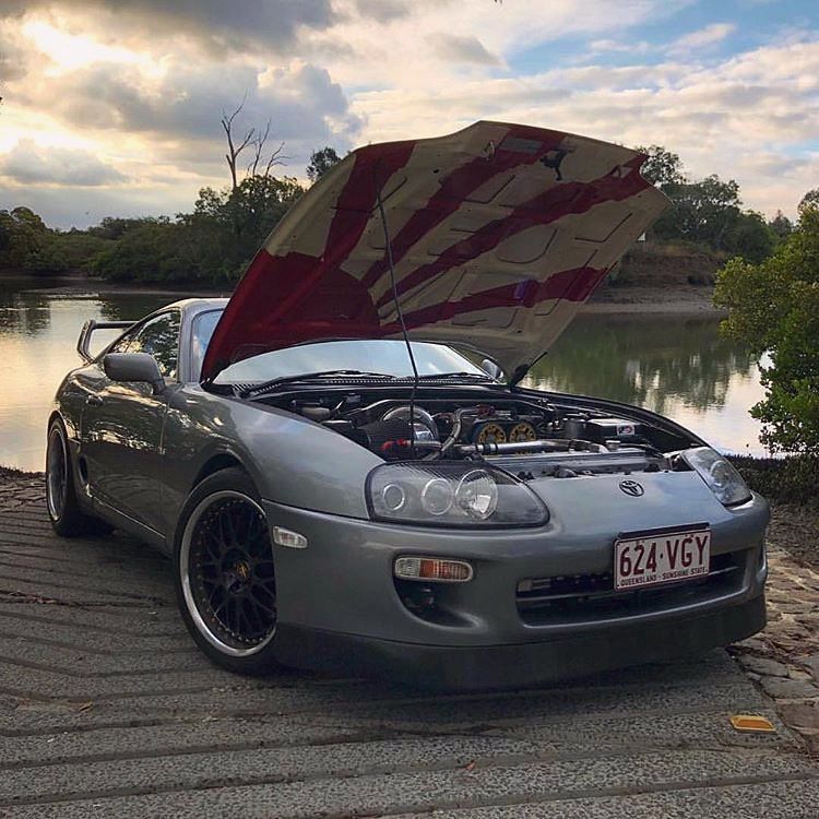 Silver sports car with hood open parked by a lakeside at dusk
