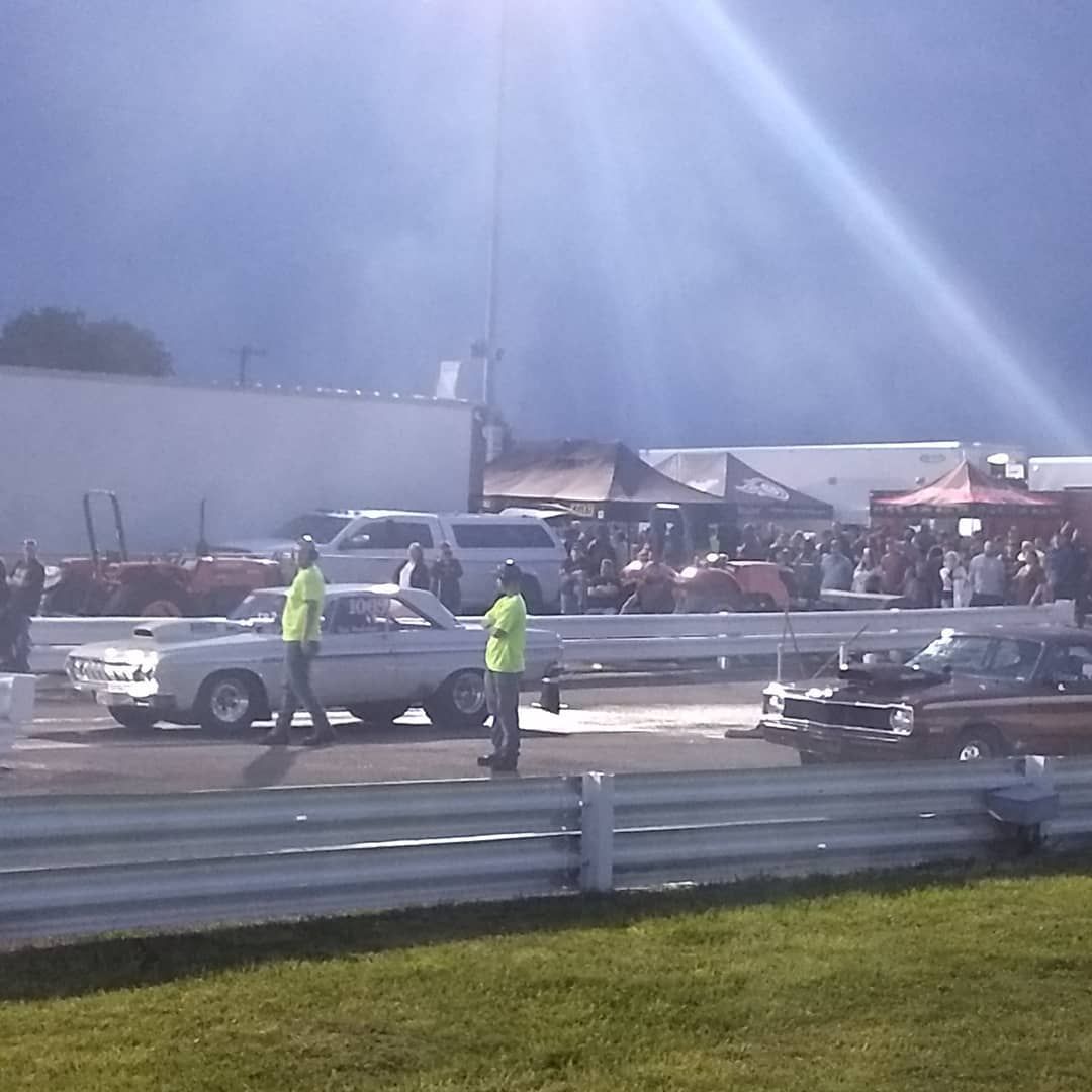 Workers in neon vests stand by a white pickup at a nighttime racetrack or fairground.