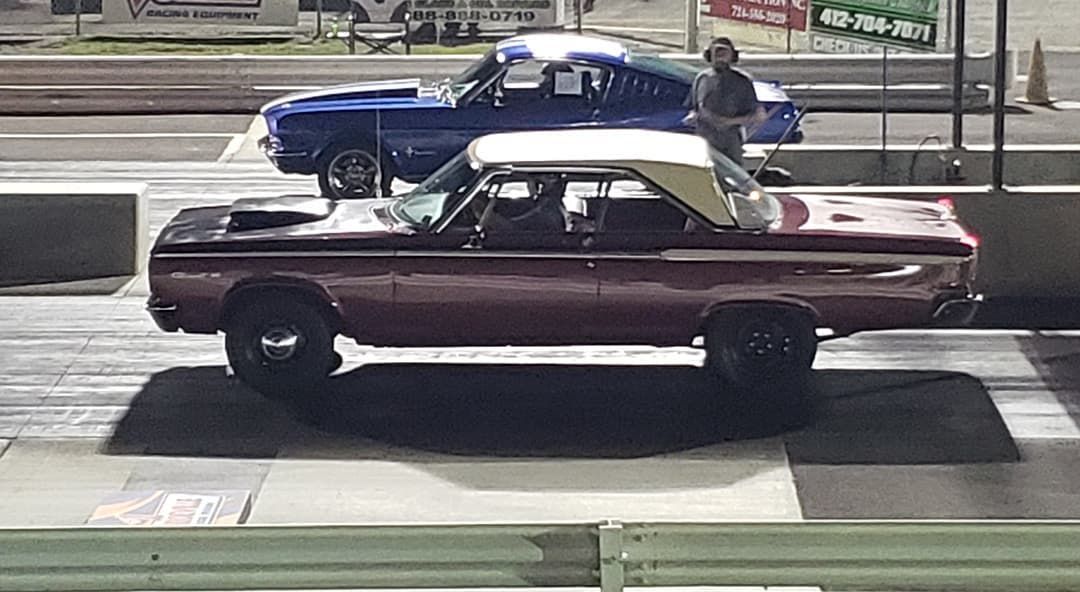 Two classic cars, a maroon convertible in front of a blue coupe, parked on a street.