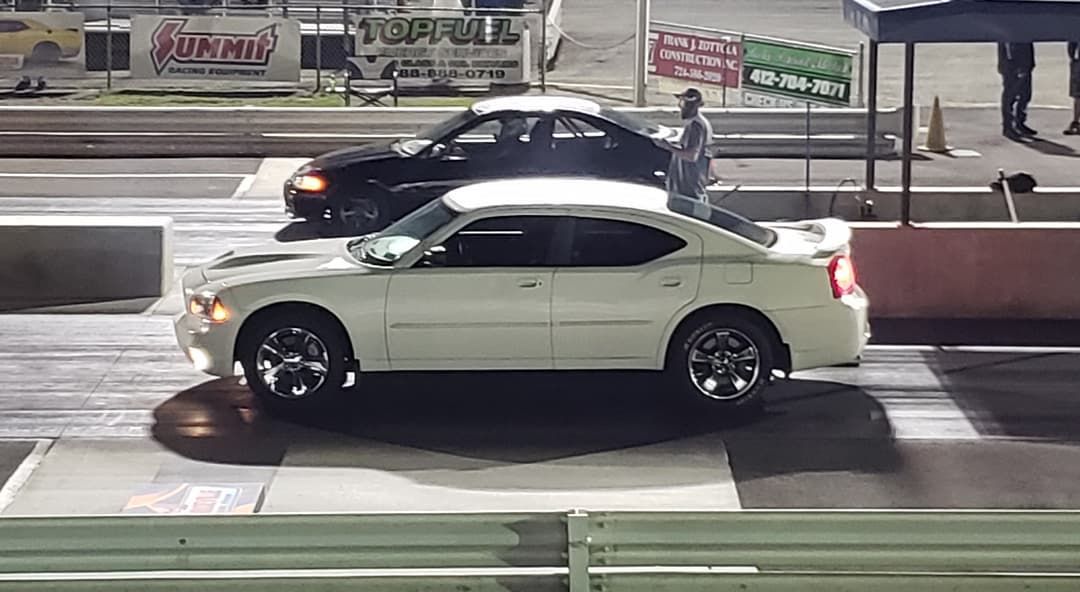 White sedan at a drag strip beside a black car under bright track lights