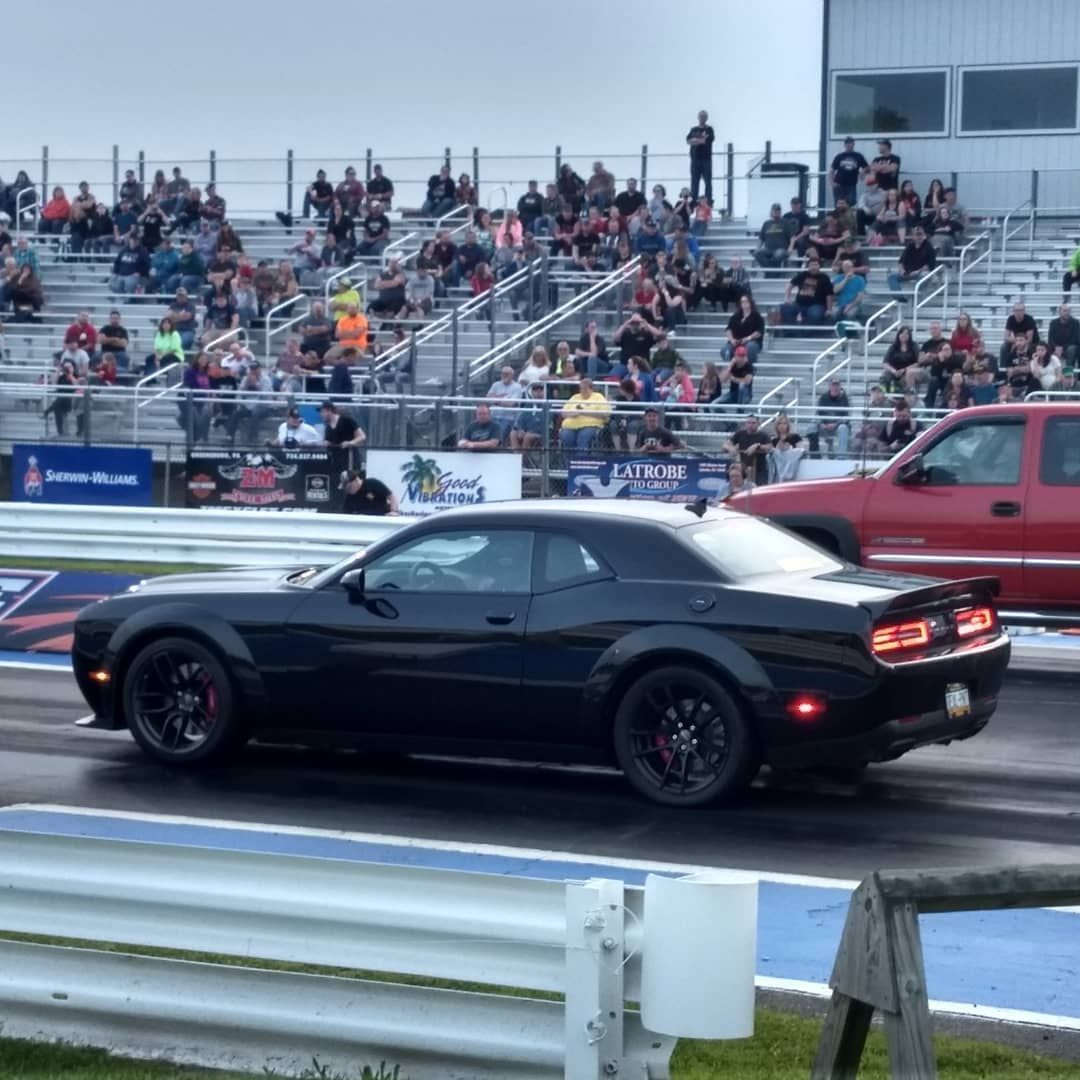 Black Dodge Challenger at a drag strip with spectators in the stands