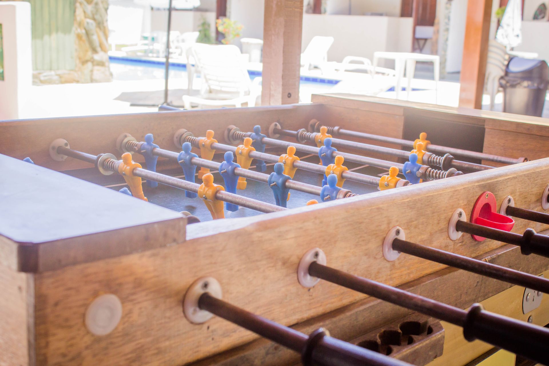 Mesa de pebolim com jogadores azuis e amarelos, perto de uma piscina.