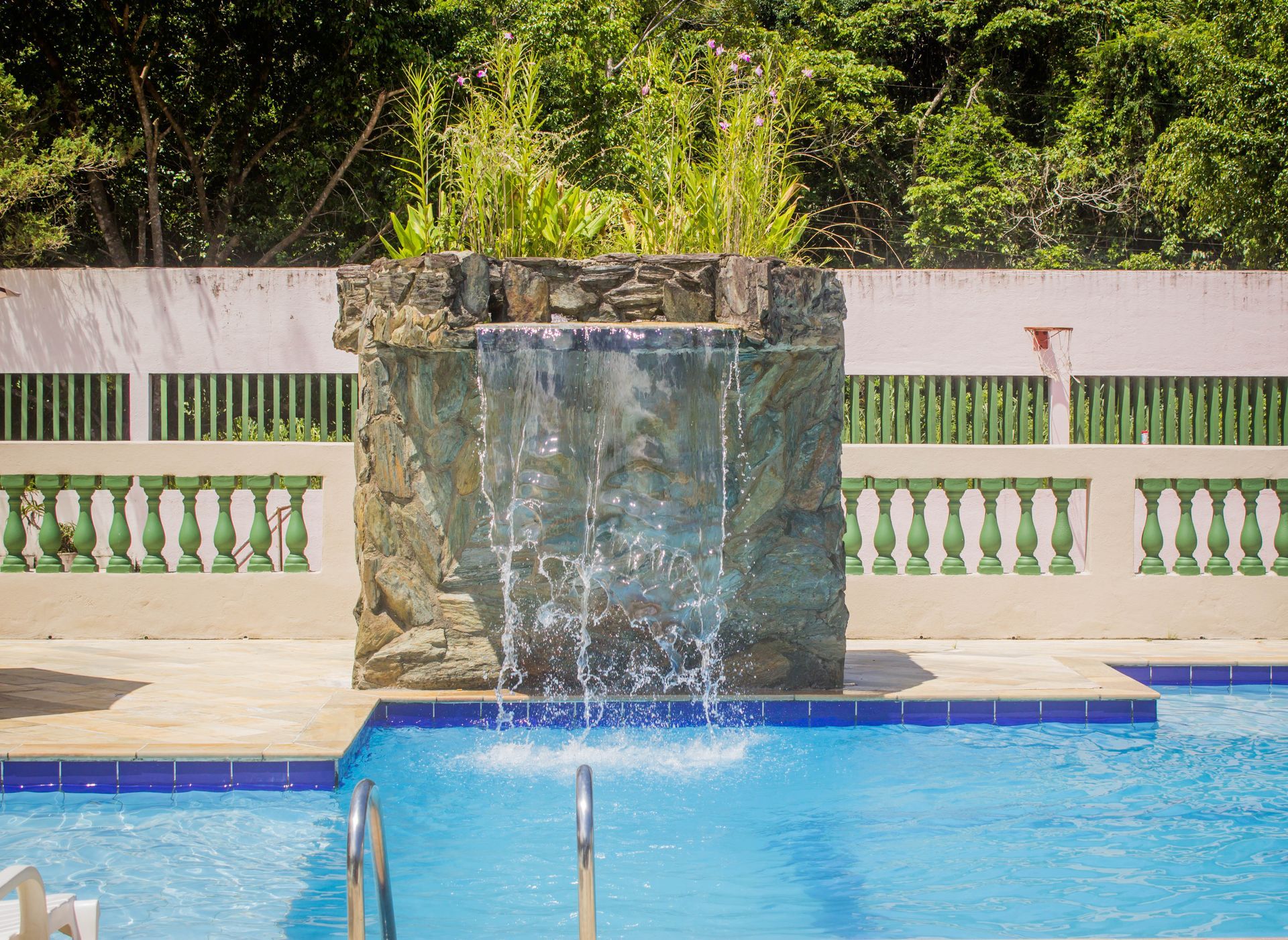 Uma piscina com cascata de pedra e árvores verdes ao fundo.