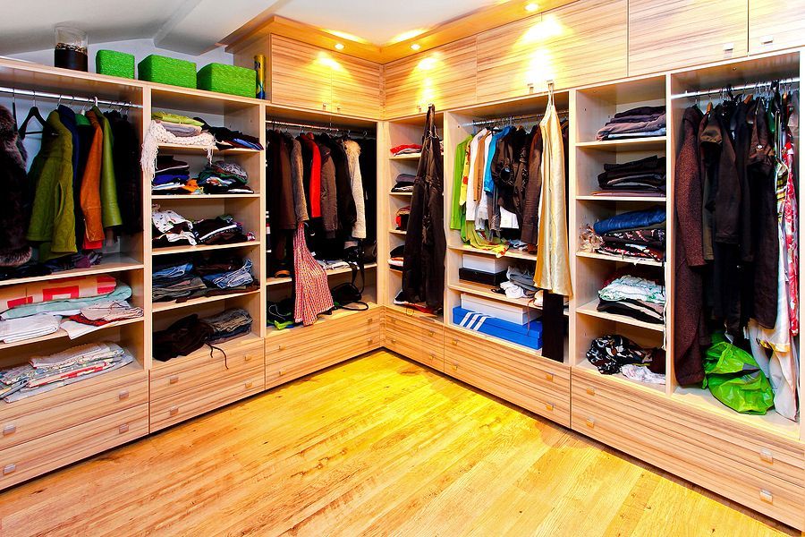 Walk-in closet with built-in shelving and clothing racks. Wood floors, various clothes and accessories stored.