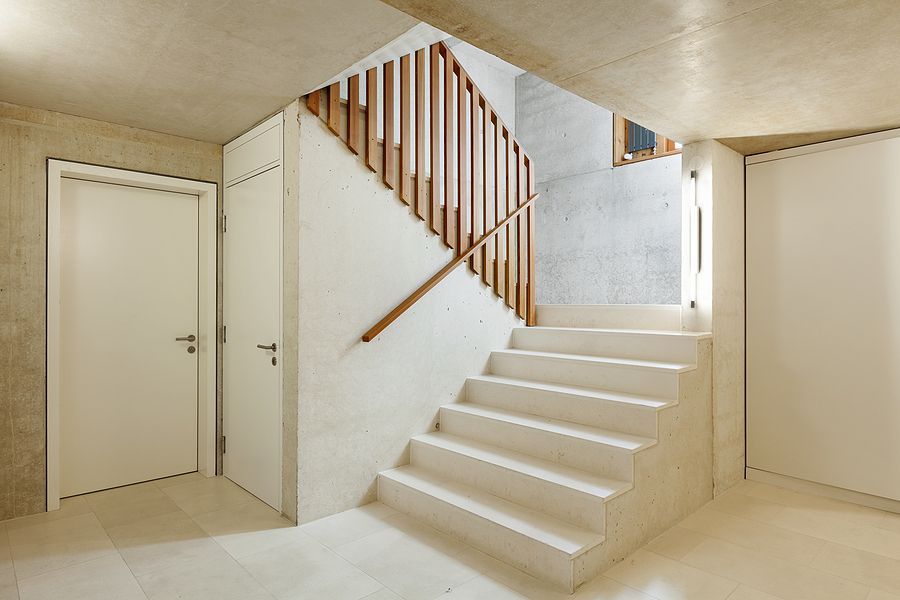 Concrete staircase with wooden railing and white walls, leading upwards.
