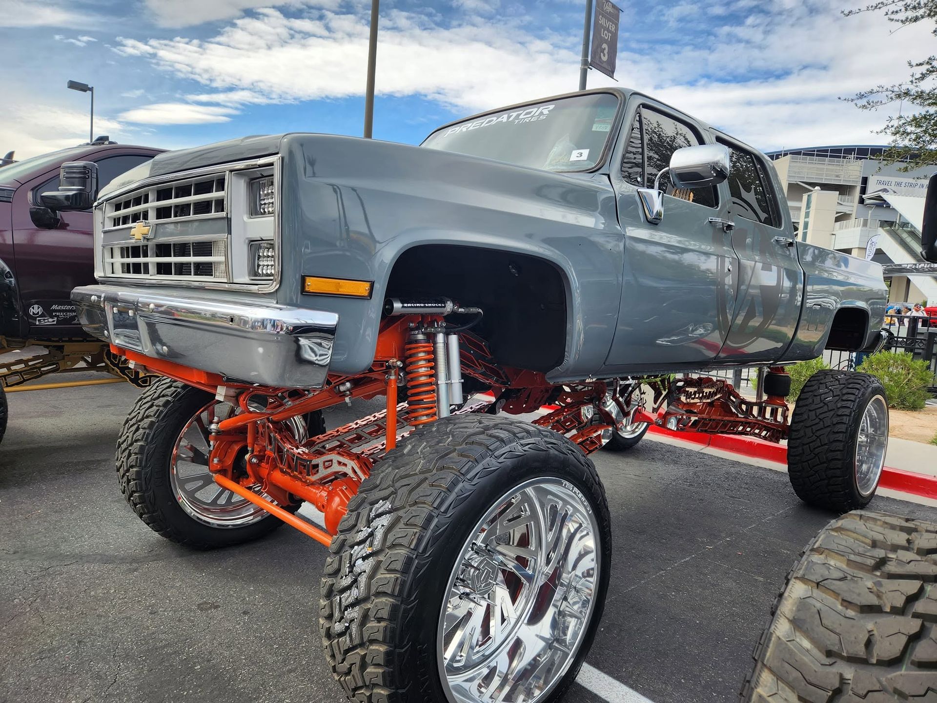 Lifted gray classic truck with orange suspension and oversized chrome wheels at a car show