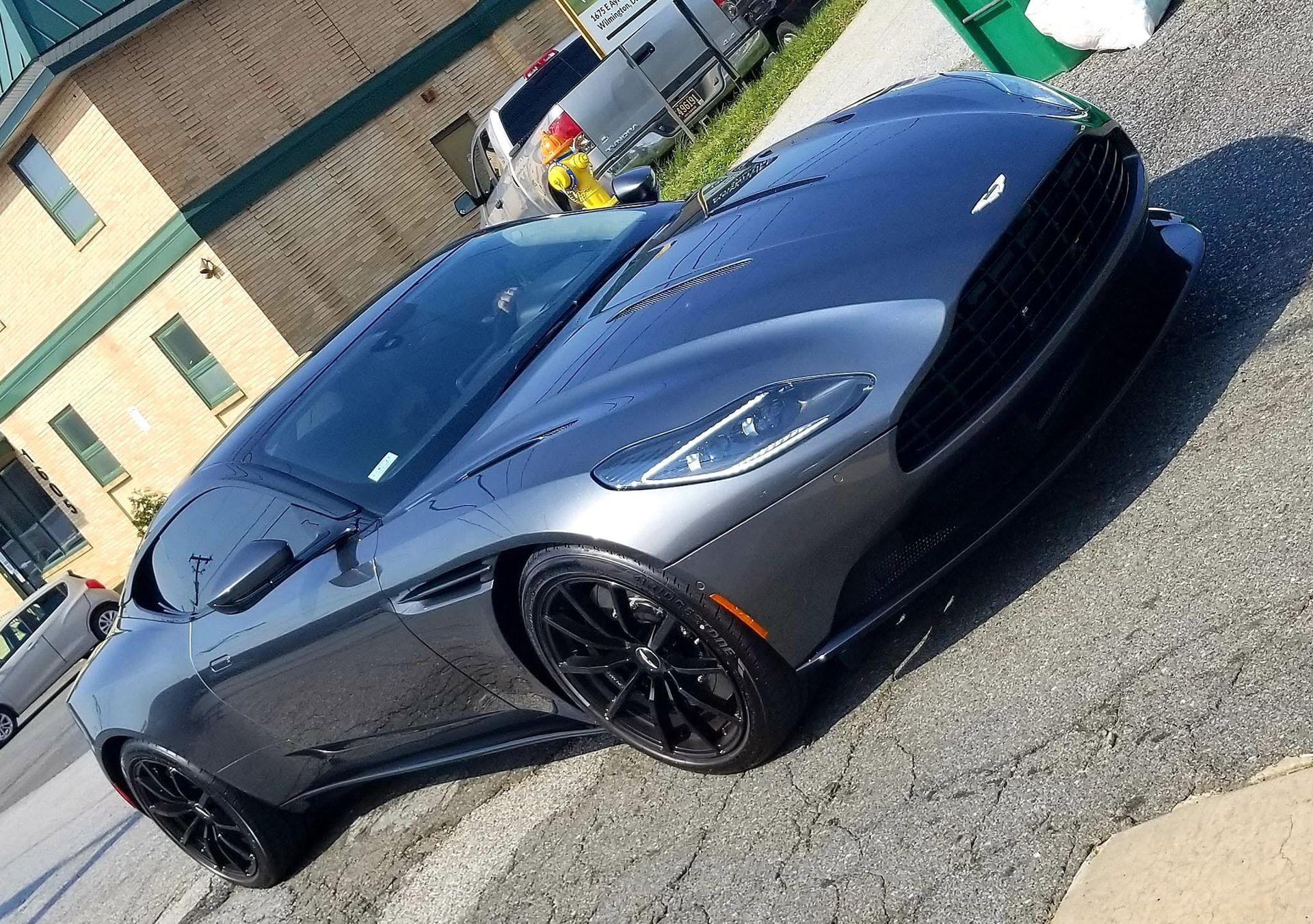 Gray sports car parked on a street, angled front view, with a person in a yellow jacket nearby.