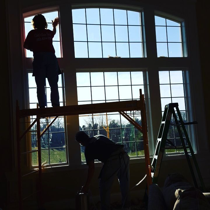 Workers installing large windows in a room, with a ladder and scaffolding in place.