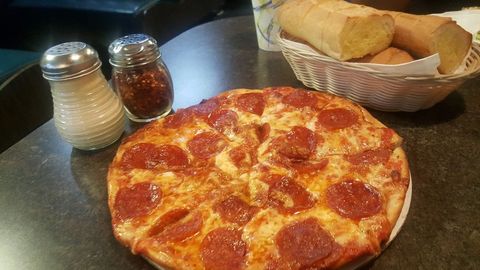 A pepperoni pizza is sitting on a table next to a basket of bread.