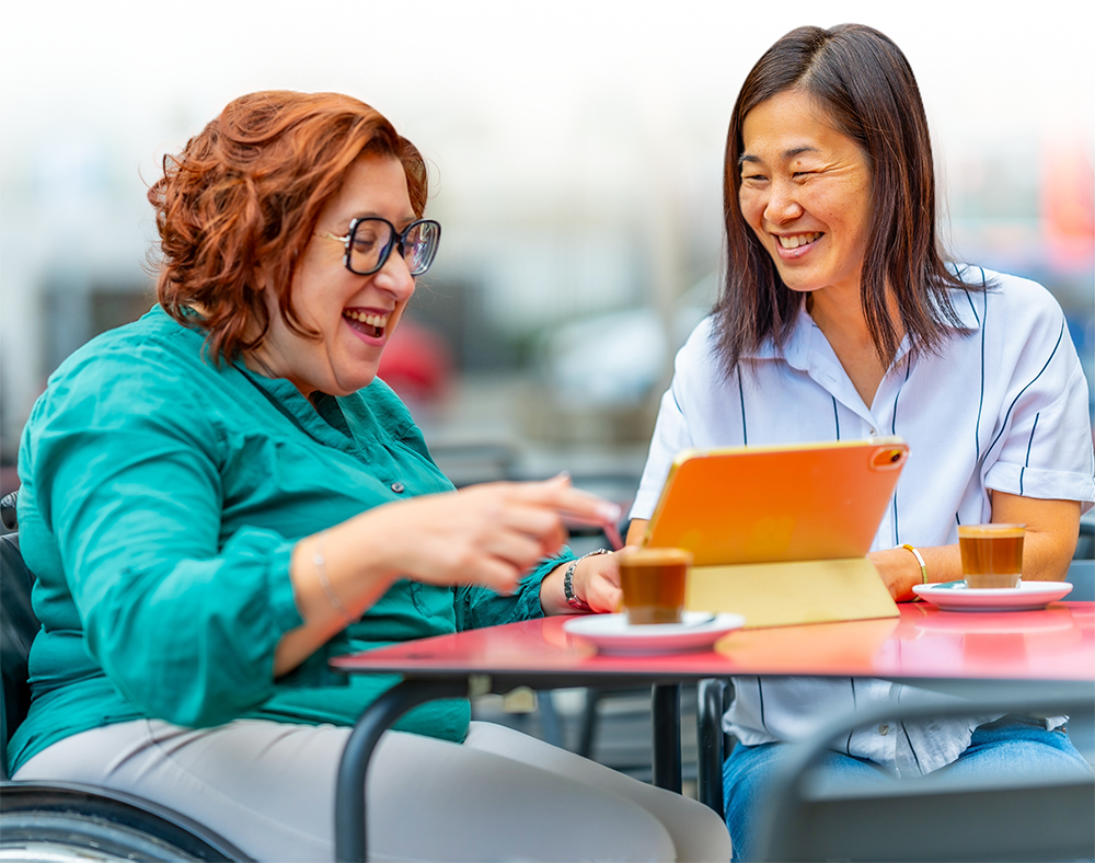 Two women are sitting at a table looking at a tablet.