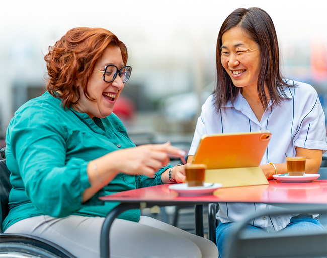 Two women are sitting at a table looking at a tablet.