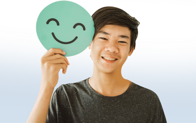 A young man is holding a smiley face in front of his face.
