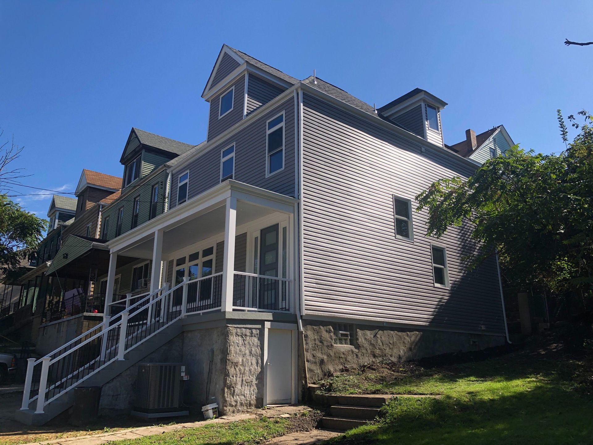 Gray house with white trim and stone foundation on a sunny hillside, seen from the side