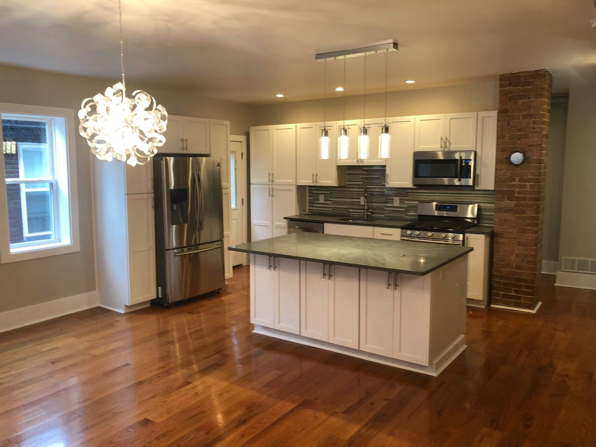 Modern kitchen with stainless steel appliances, white cabinets, island, and hardwood floors