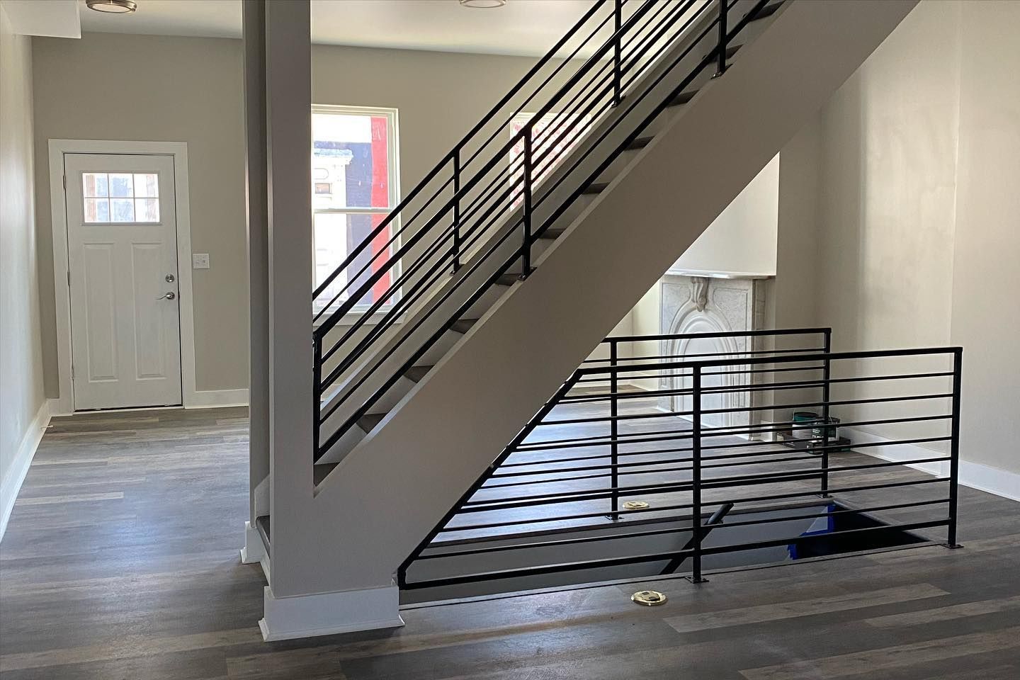 Empty indoor stairwell with black metal railing and white walls, hardwood floor, and a white door on the left.