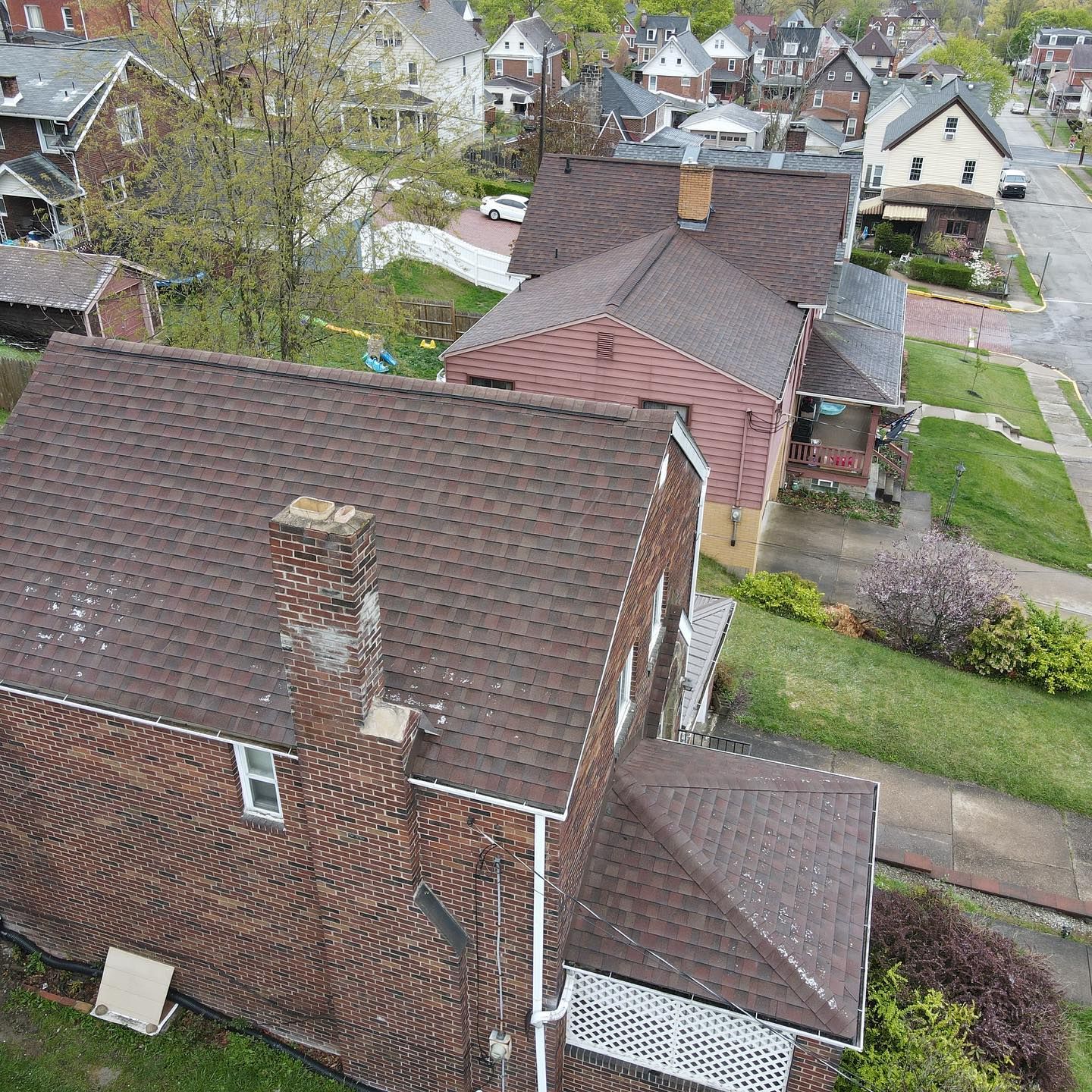 Aerial view of brick houses, brown roofs, and a suburban neighborhood street.