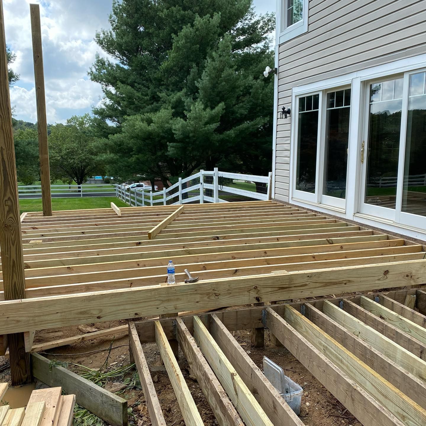 Partially built wooden deck beside a house, with exposed joists in the foreground and white railing in back