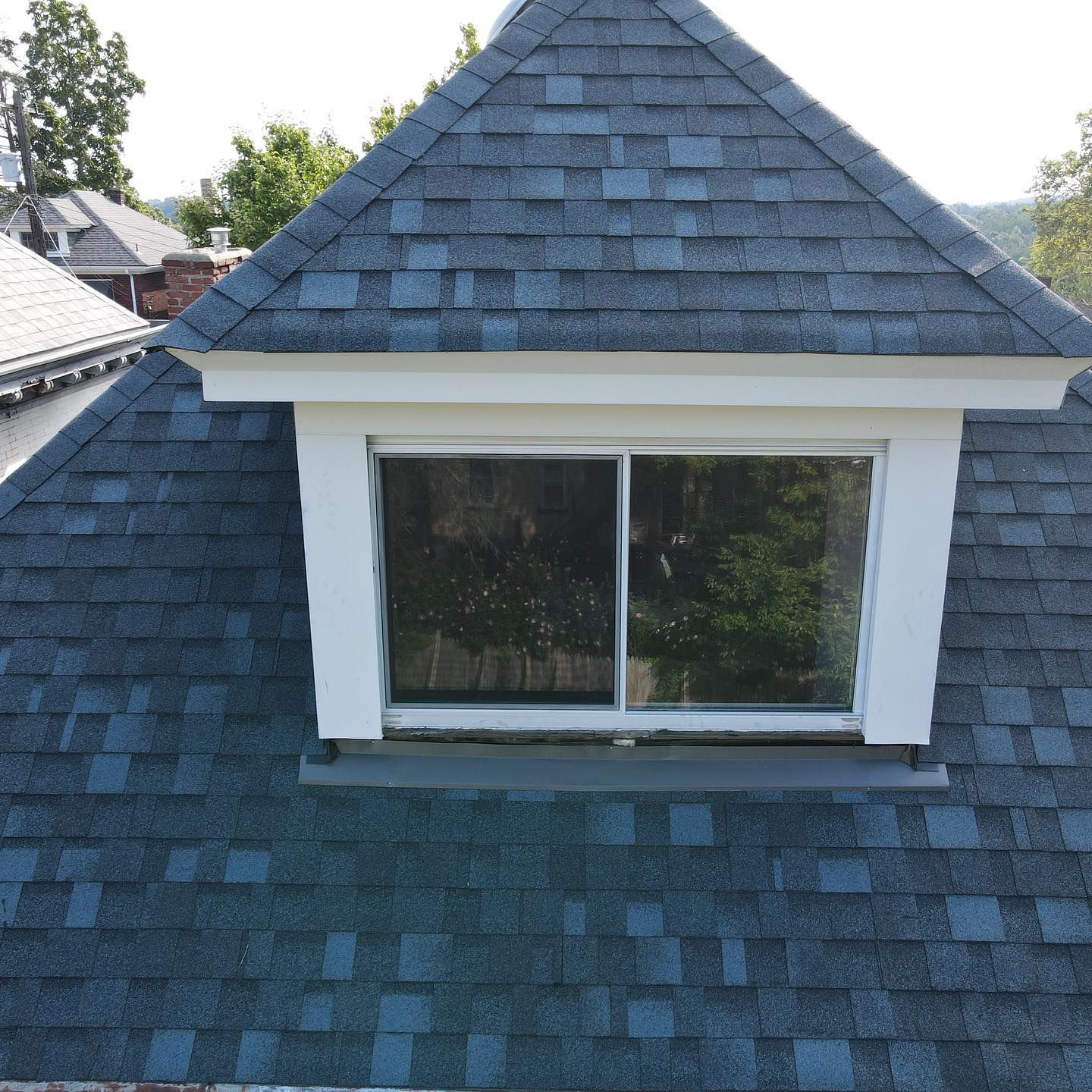 Blue-shingled dormer window on a house roof under a clear sky