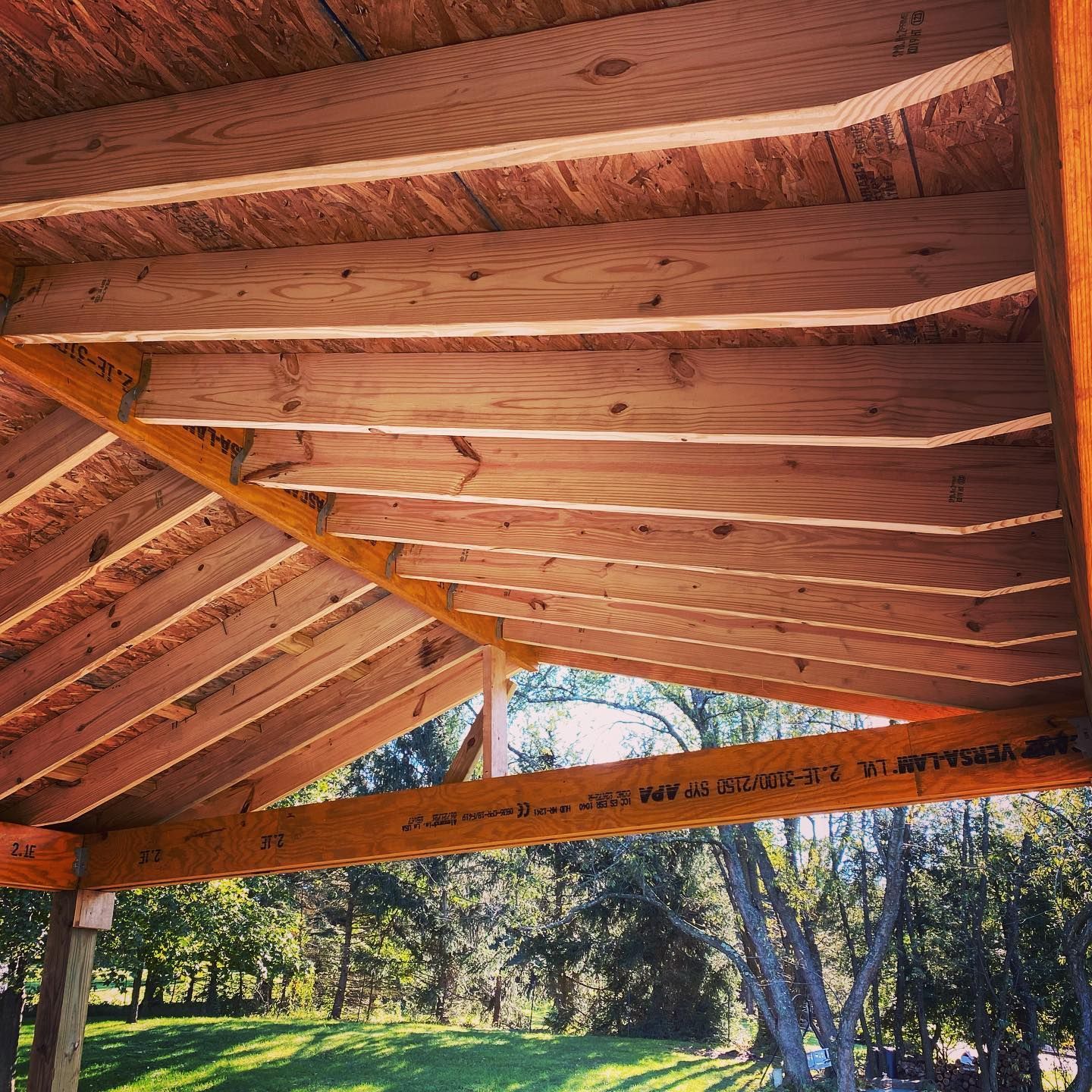 Wooden porch roof with exposed beams overlooking a sunny yard and trees
