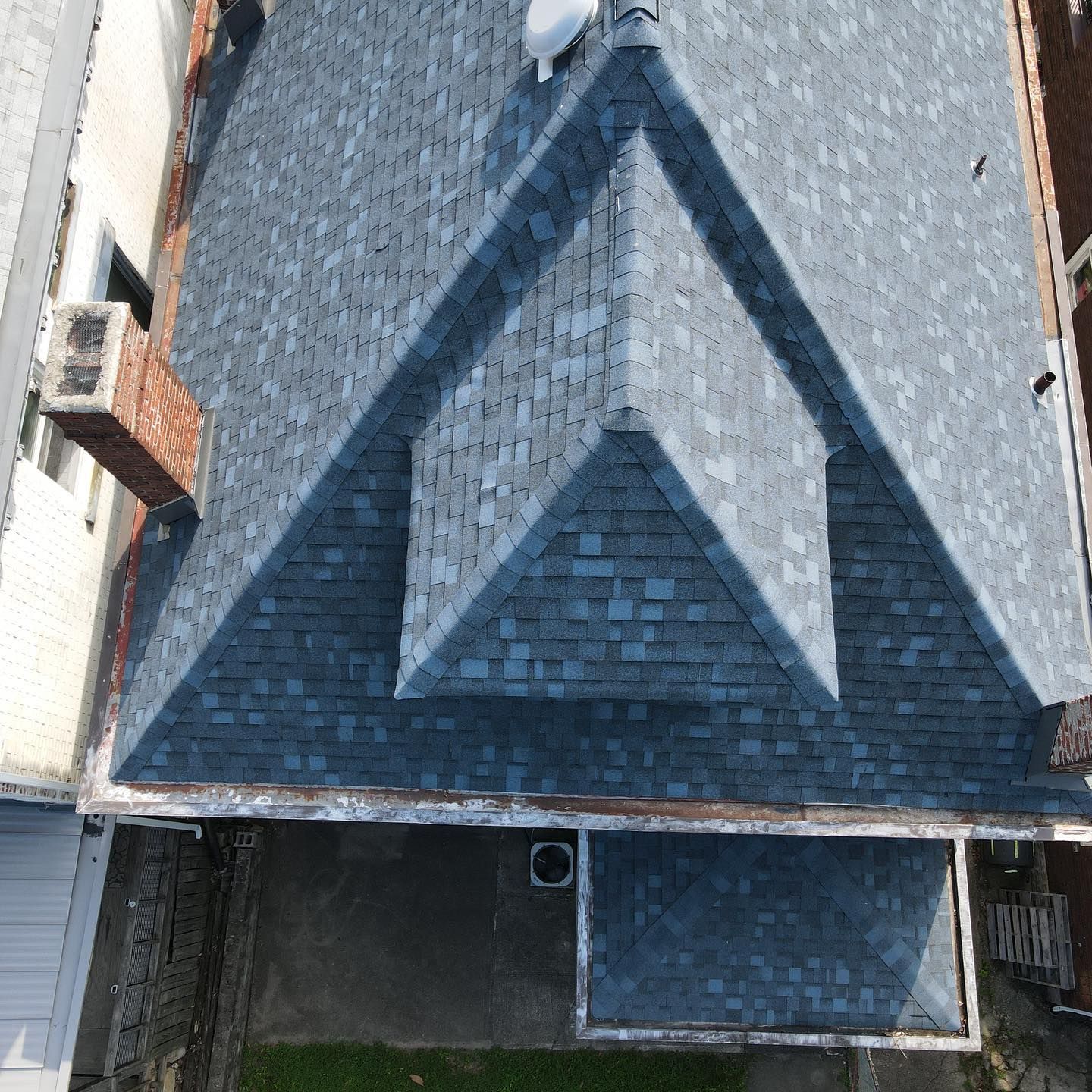 Aerial view of a dark gray shingled roof with a large triangular pattern and neighboring buildings.