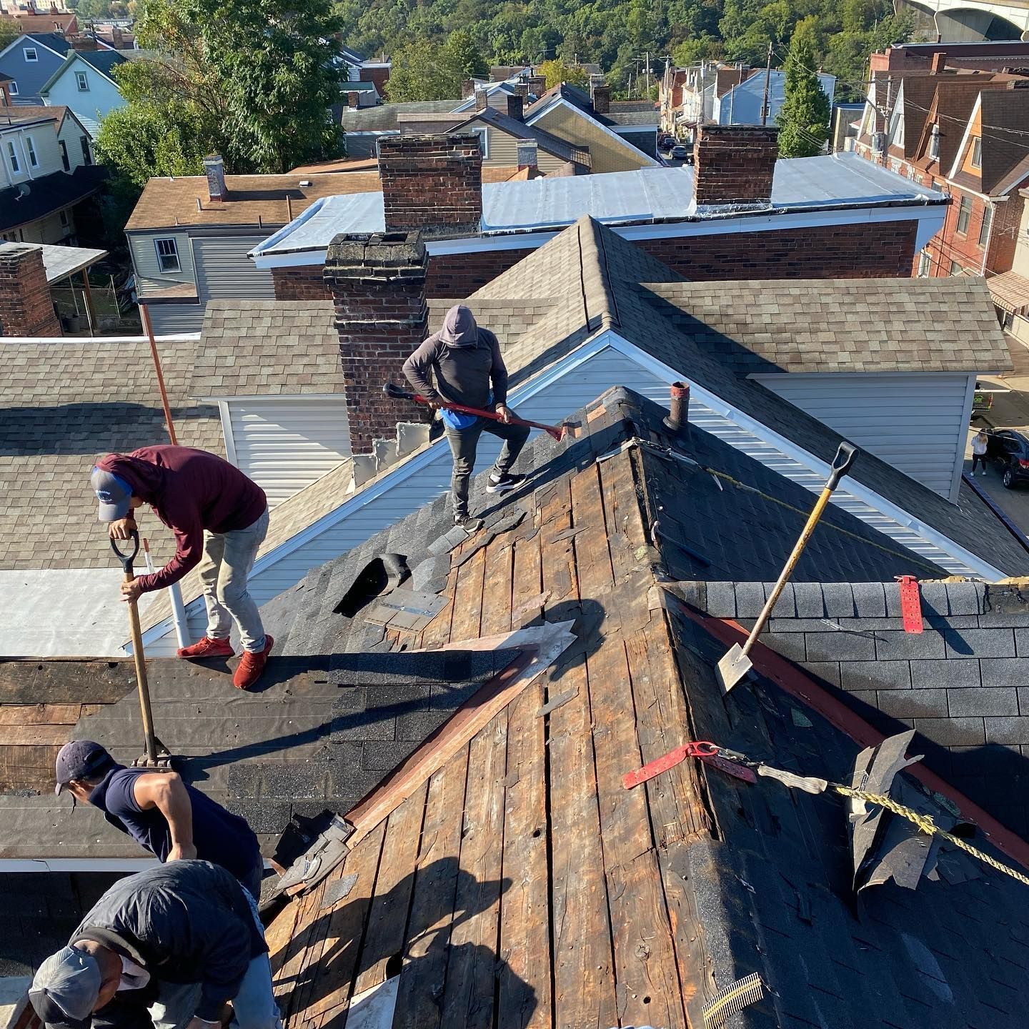 Roofers repairing a steep shingled roof with tools and safety harnesses on a residential house