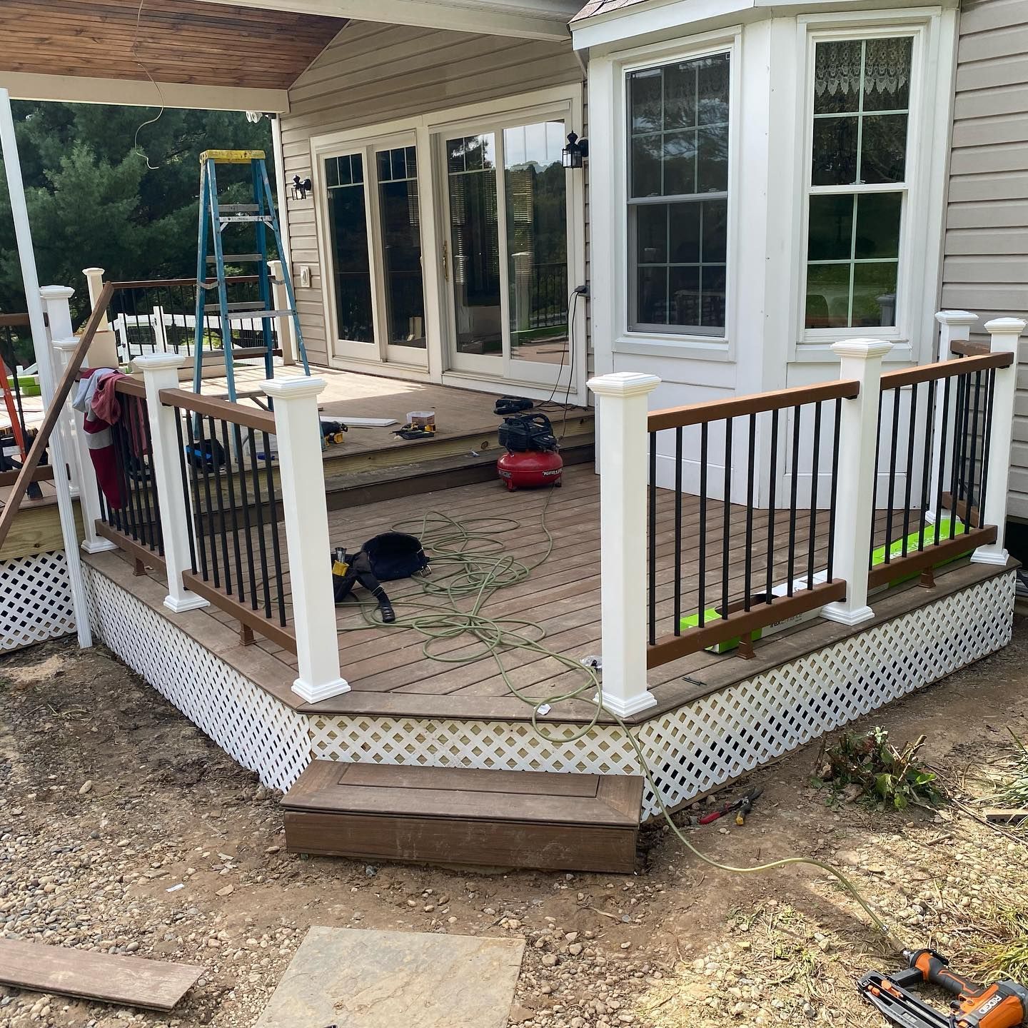 Back porch deck under construction with white railings, wood columns, and tools on a brick floor