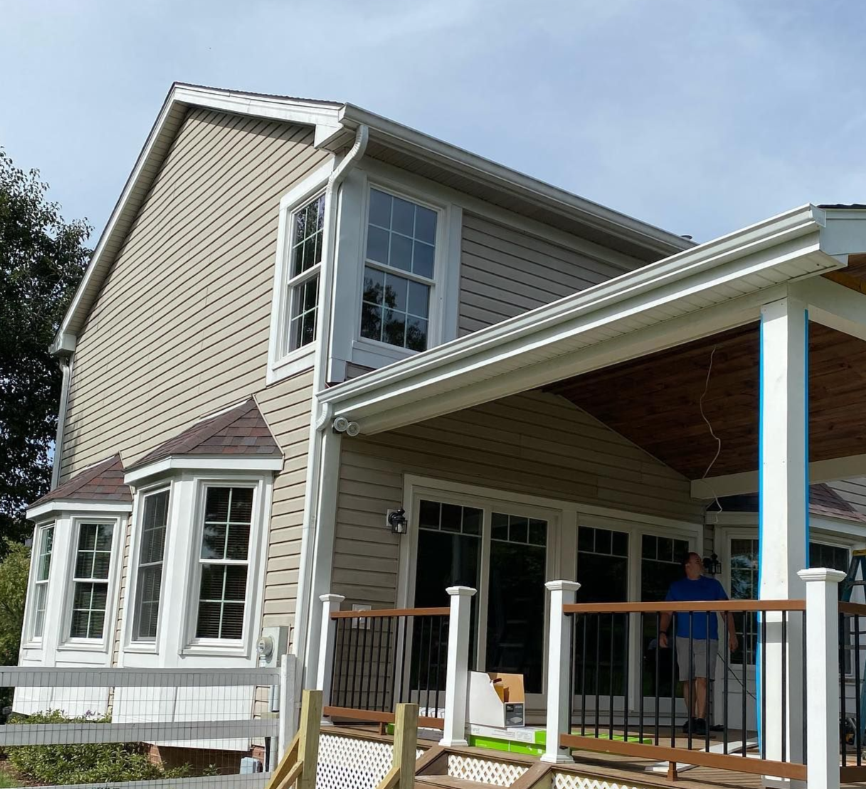 Two-story beige house with a covered porch and a person standing inside the entrance