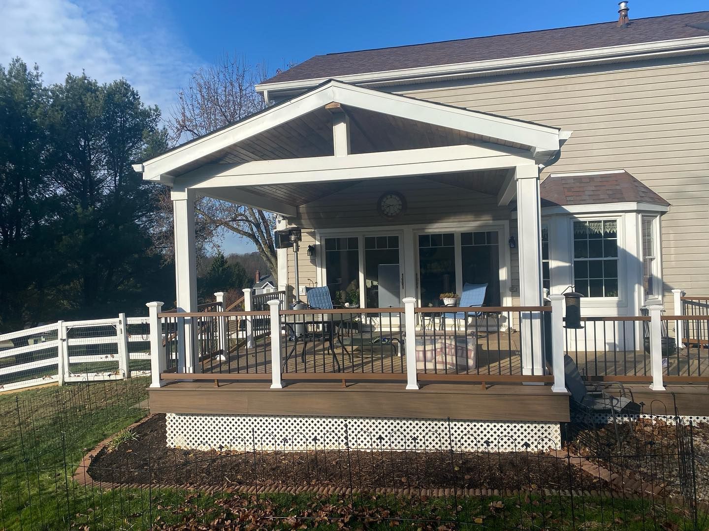 Front porch with white railing and covered seating area on a light-colored house under a blue sky