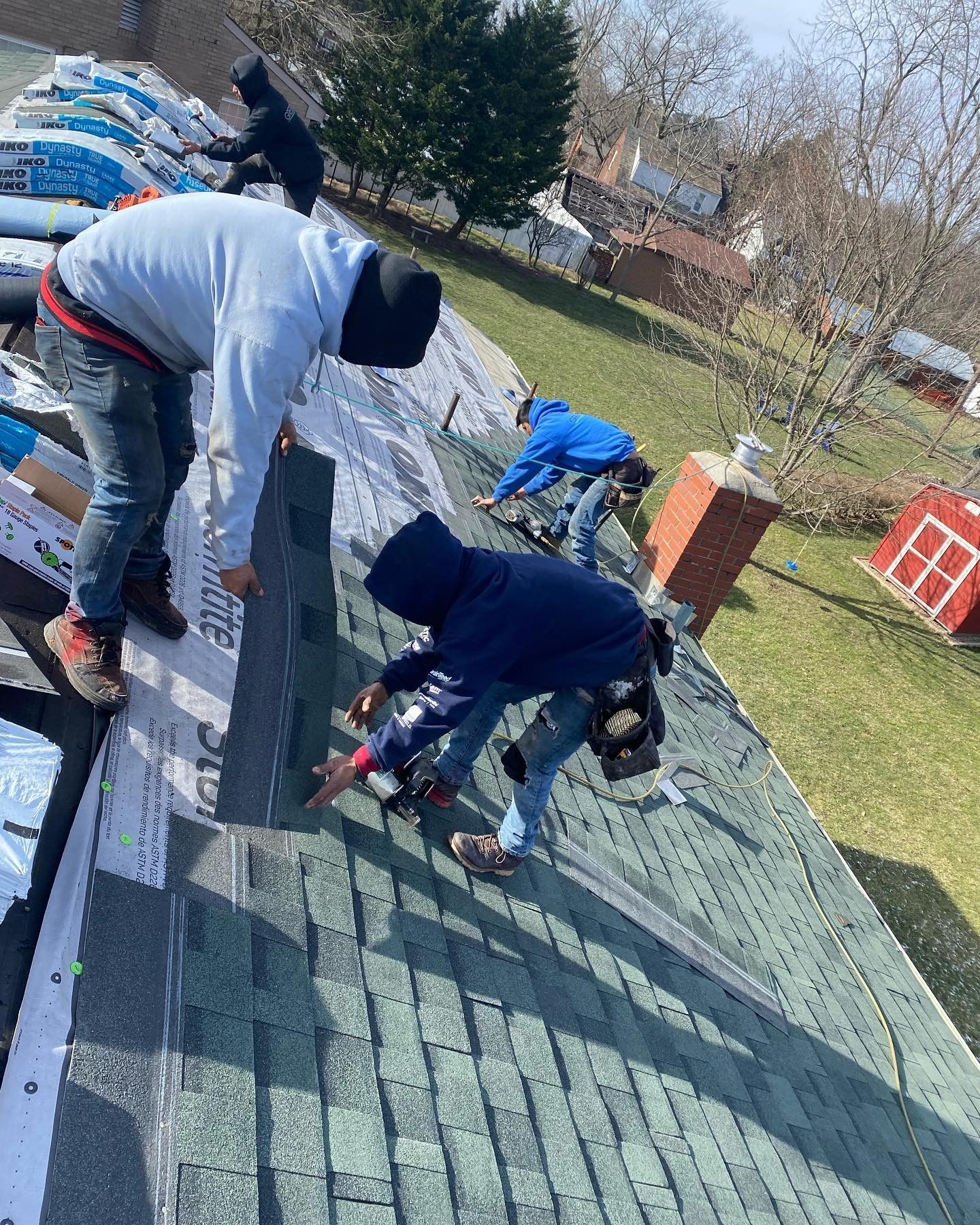 People working together to repair a green shingled roof outdoors
