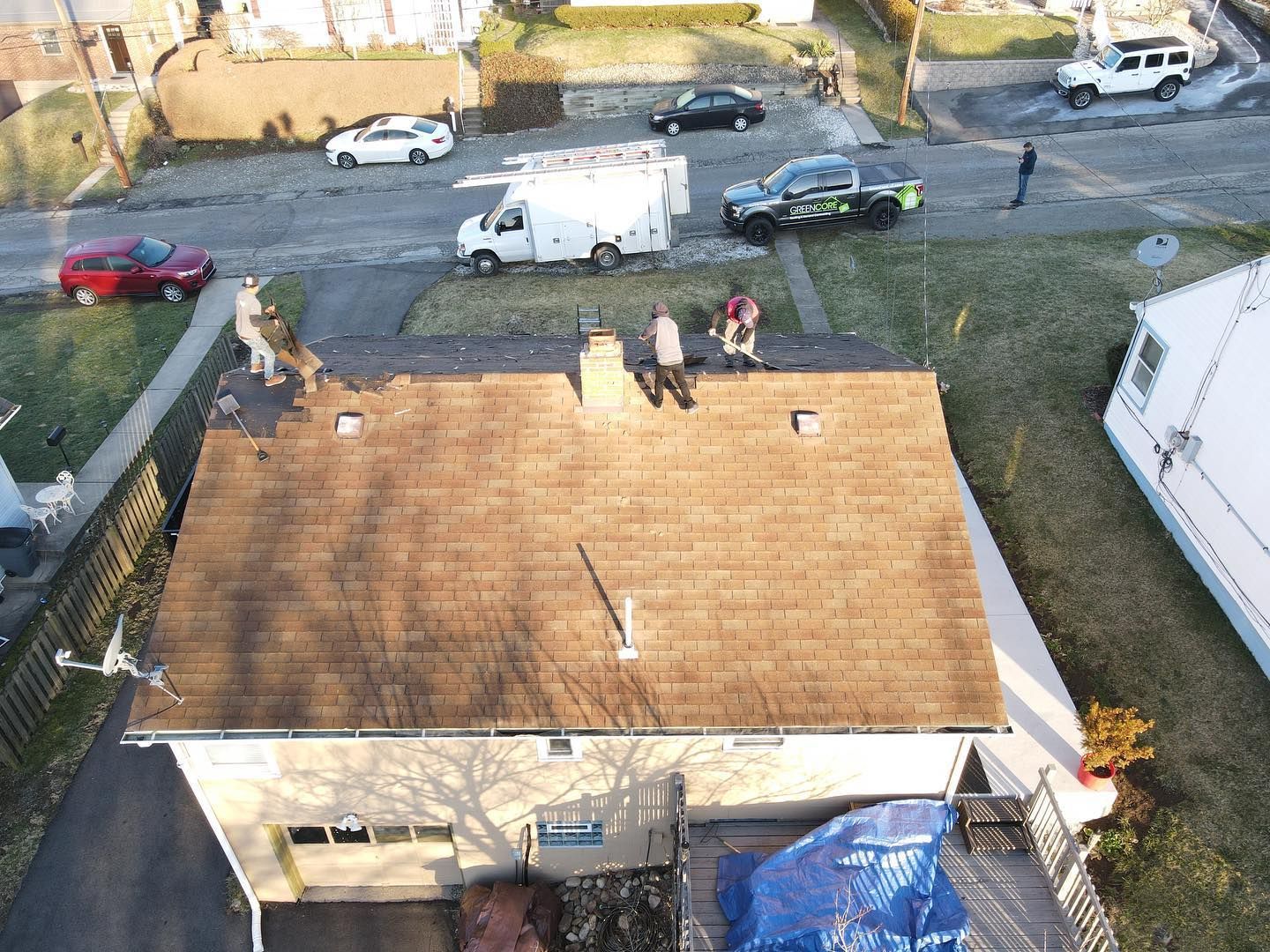 Aerial view of workers on a brown roof beside parked cars and a street.
