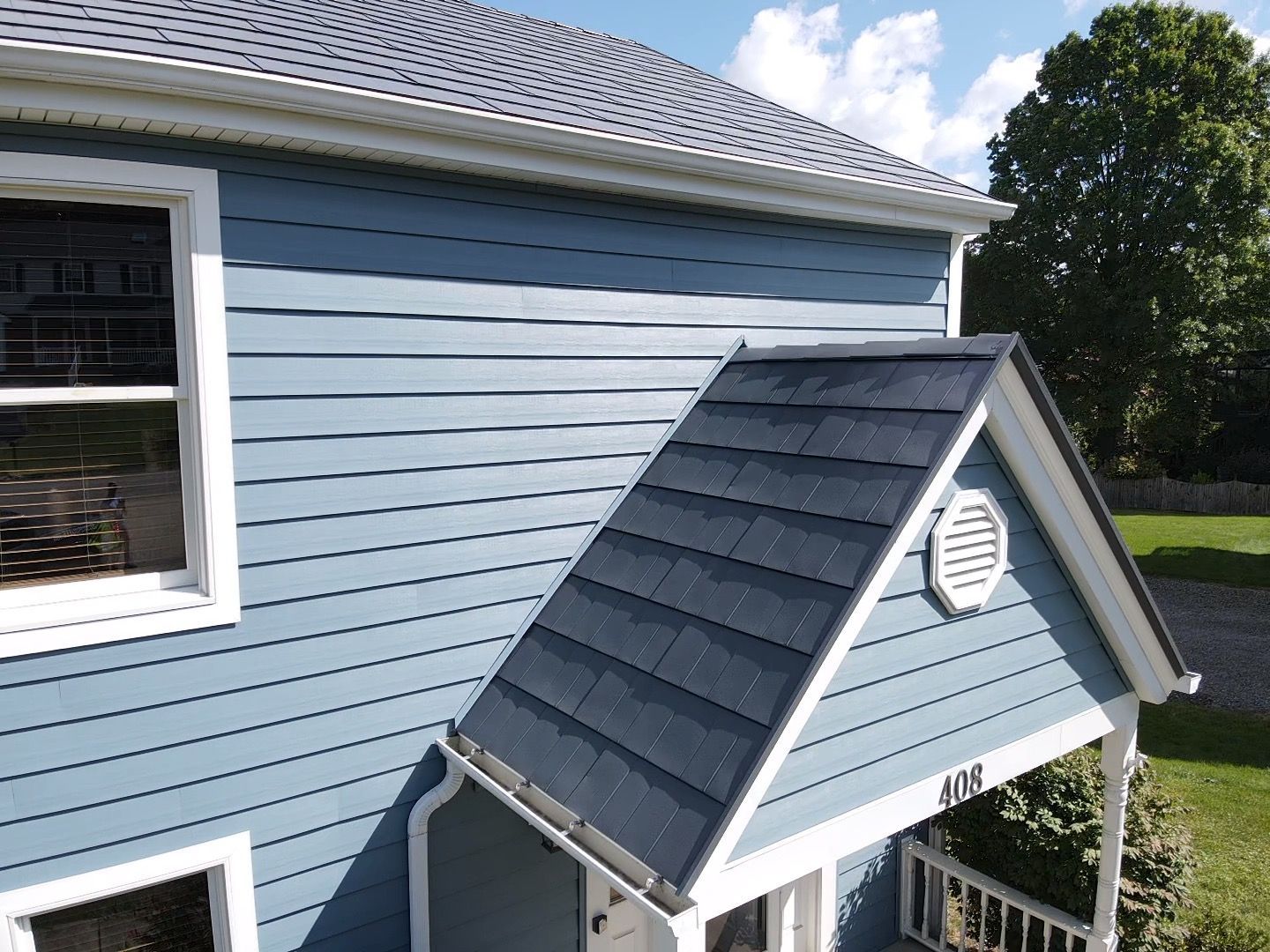 Blue house exterior with a small gabled entry roof and round vent