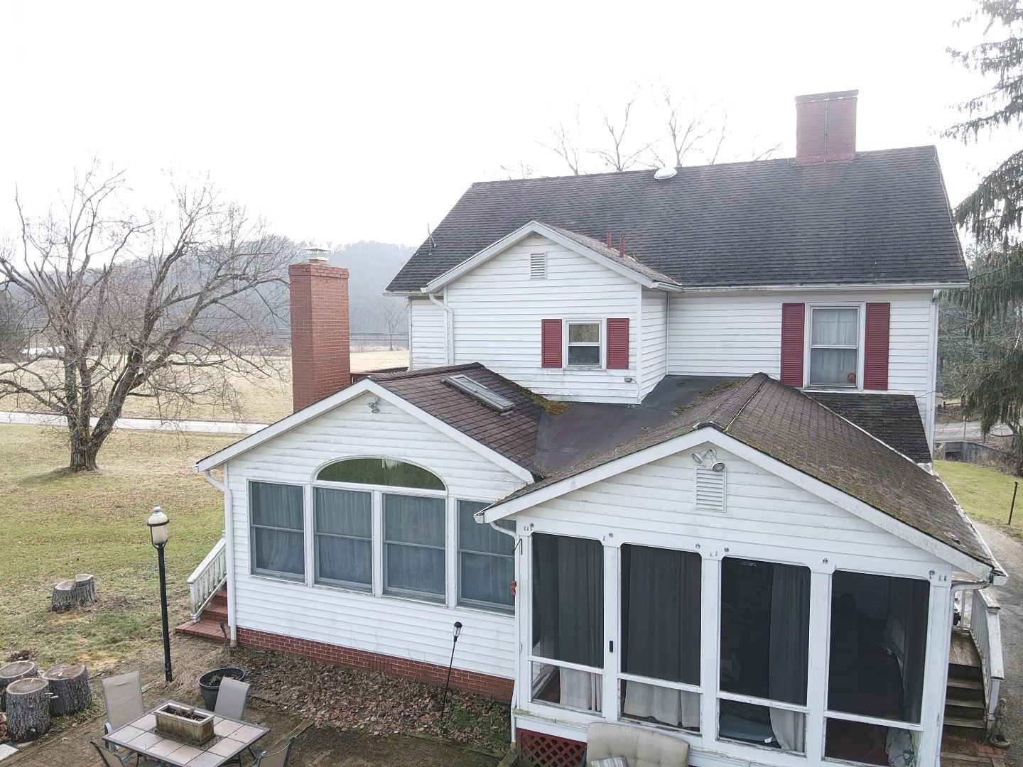 White house with screened porch and red shutters beside a cloudy yard and leafless trees.