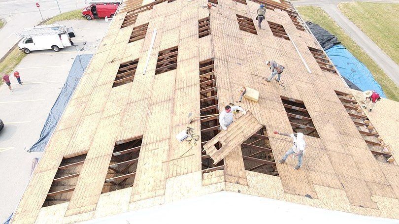 Workers installing plywood roofing on a house roof under construction, with several roof openings visible.