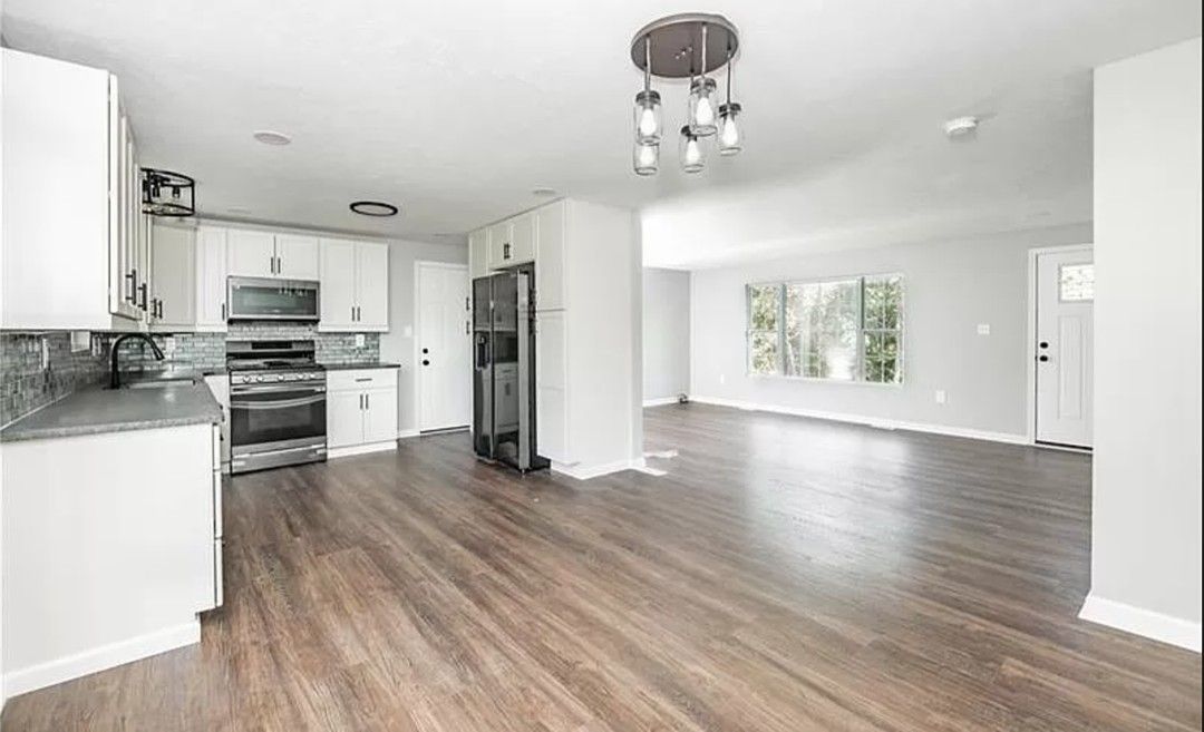 Bright empty modern kitchen and living room with wood floors and white walls