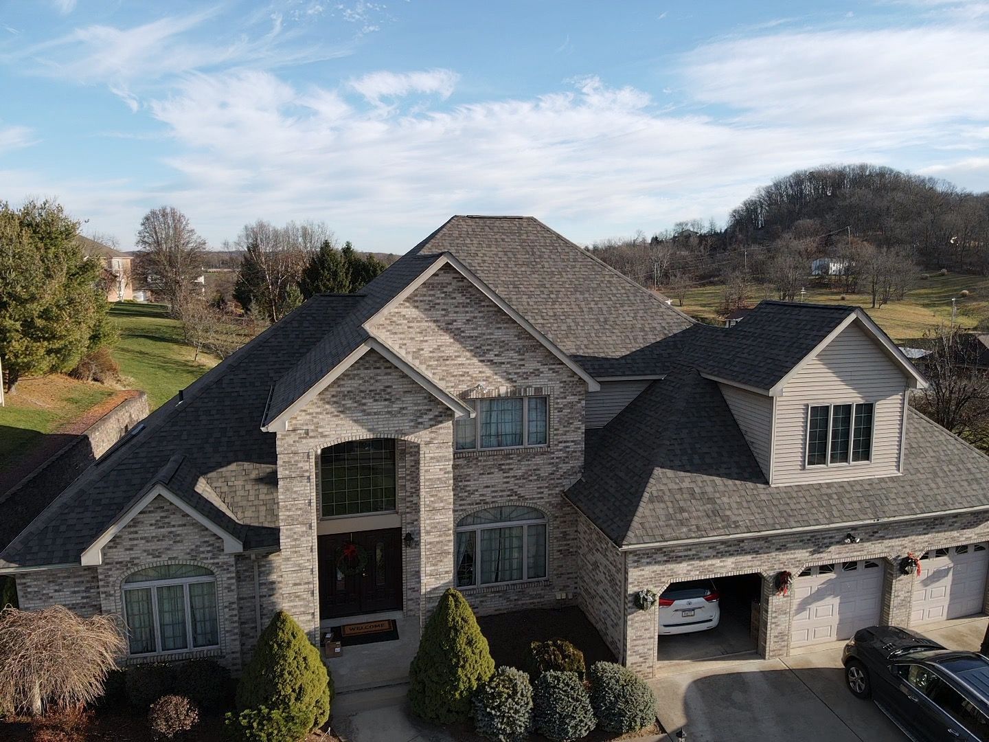 Large gray stone house with multiple gables, dormer windows, and a three-car garage in a suburban setting