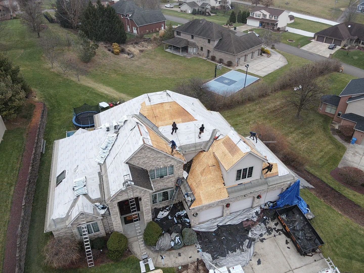 Aerial view of a house roof under repair, with exposed plywood and workers on top.