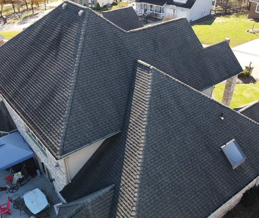 Aerial view of a dark gray shingled house roof with multiple gables and skylight
