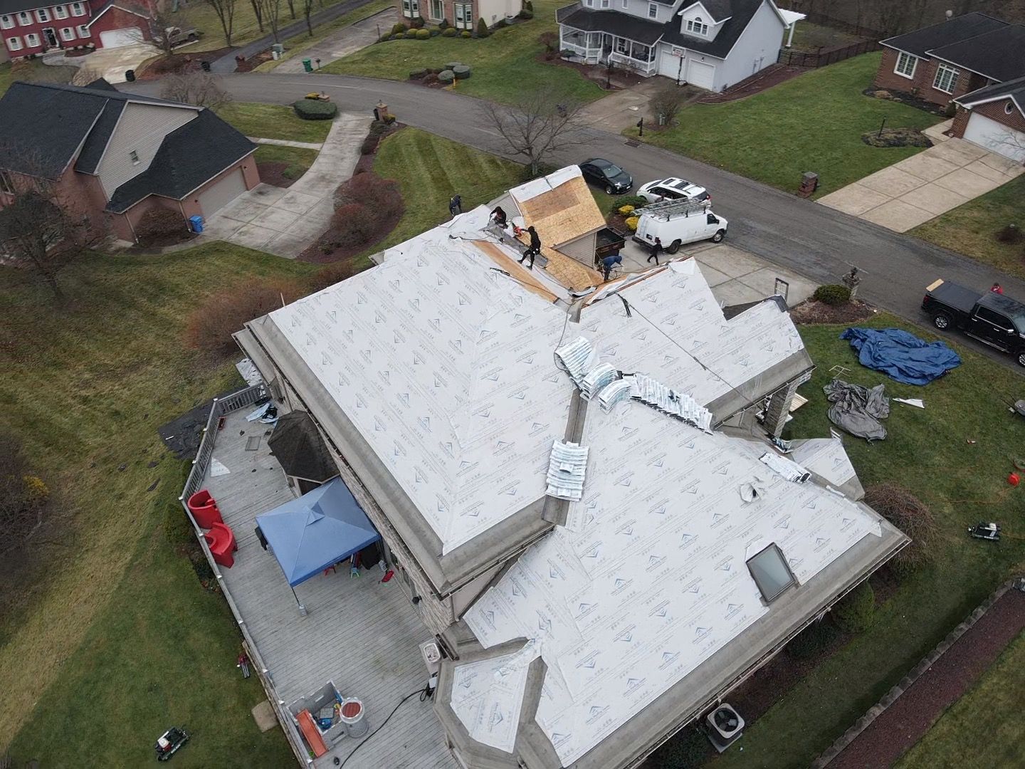 Aerial view of a roof with storm damage and construction materials on a suburban house.