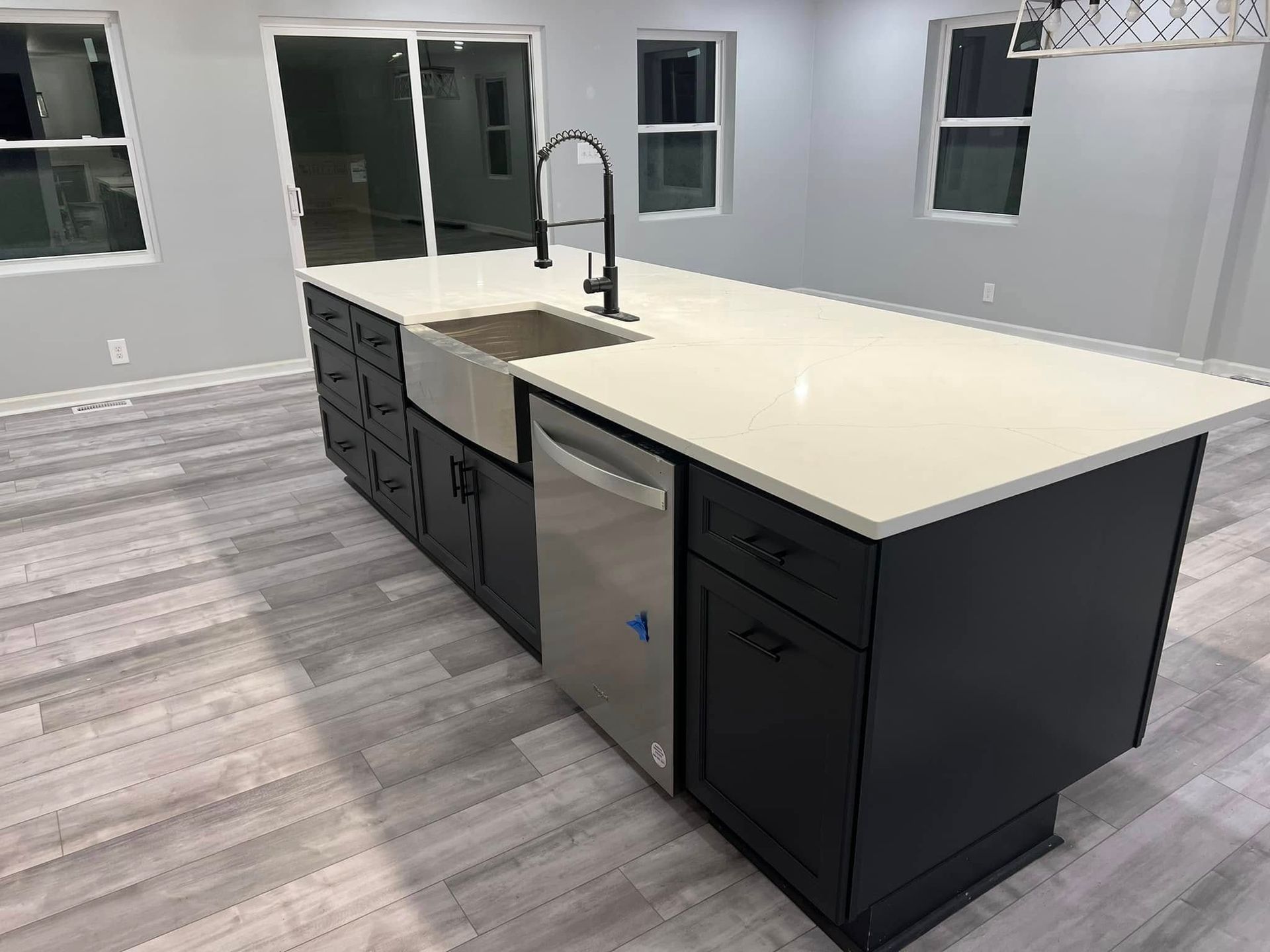Modern kitchen island with white countertop, black cabinets, sink, and stainless dishwasher in a bright room