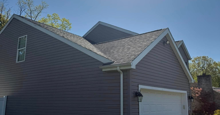 Side view of a gray house with a gabled roof, white trim, and a white garage door under a blue sky